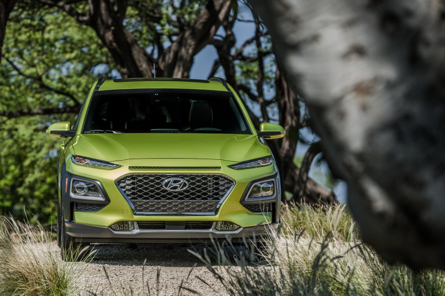 a bright green Hyundai Kona crossover SUV rests in a heavily treed parking lot