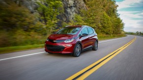 Red 2019 Chevrlet Bolt EV hatchback driving down the road next to a forest