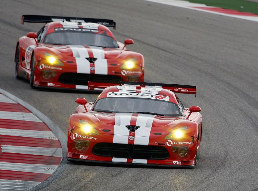 Two red Dodge Vipers with white racing stripes race around a track