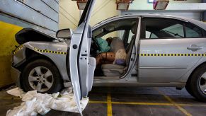 A crash test dummy sits behind a deployed airbag inside a damaged Hyundai Sonata