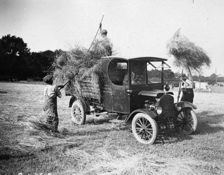 Men loading hay into the back of the back of an old pickup truck.