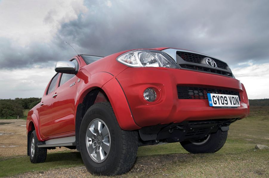 A red Toyota Hilux driving up a hill.