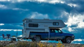 An older pickup truck with a camper in the bed parked on a road.