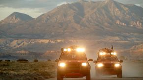 Two off-road trucks with light bars drive down a highway.