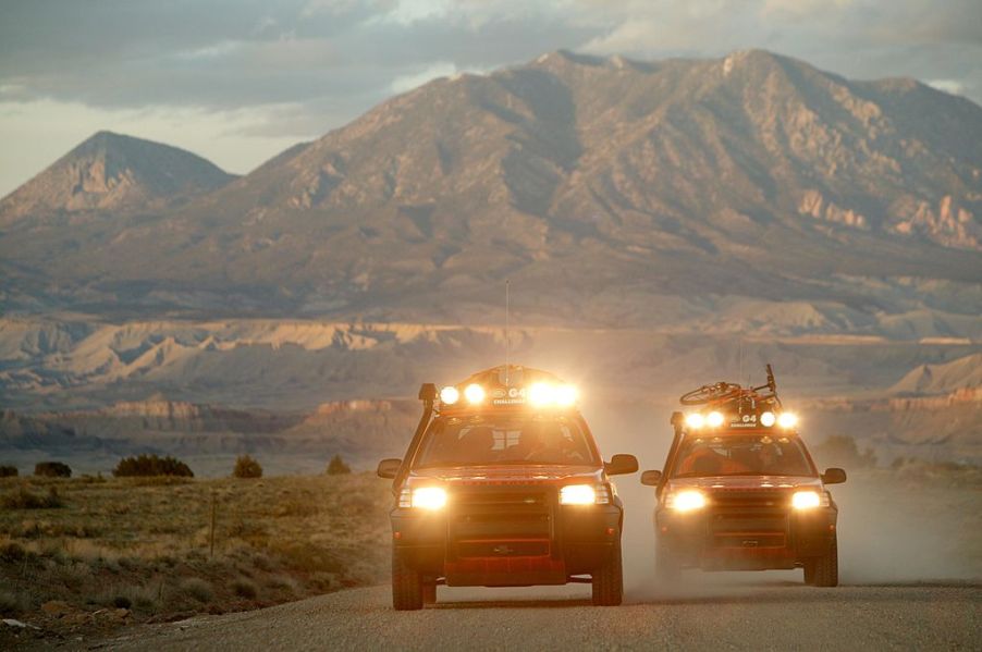 Two off-road trucks with light bars drive down a highway.