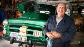 An older man standing next to a truck that he is restoring.