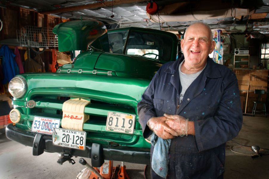 An older man standing next to a truck that he is restoring.