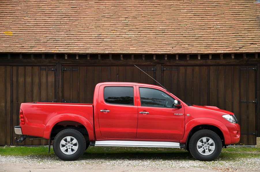 A red Toyota pickup truck parked in front of a fence.