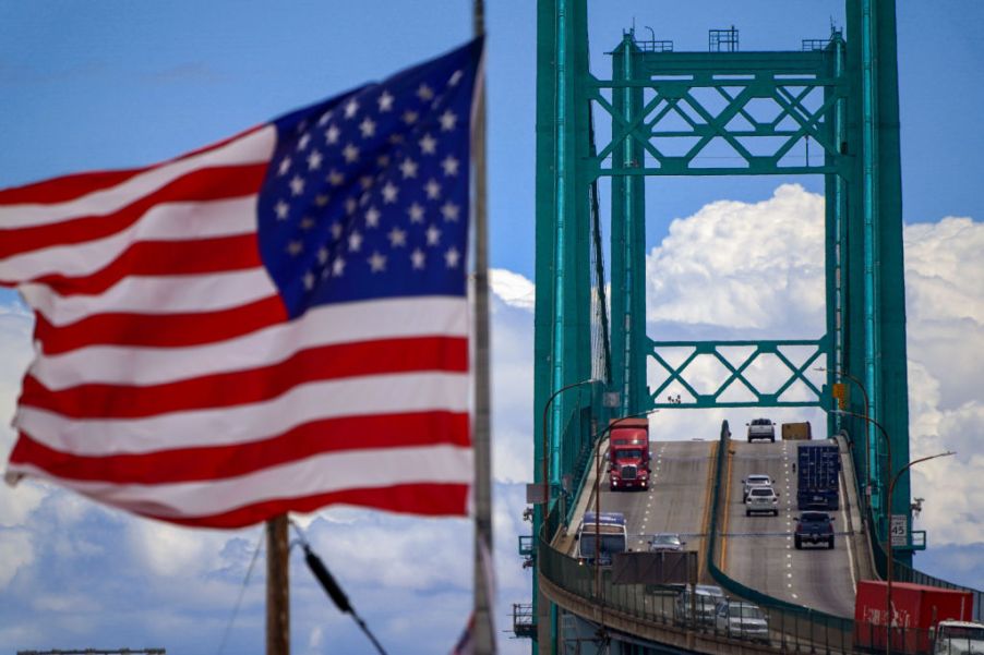 An American flag waves as cars and trucks go over a bridge.