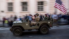 A military Jeep drives down the street with an American flag