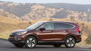 The 2015 Honda CR-V compact SUV model with a dark reed paint color option parked on an asphalt road near hills of yellow grass