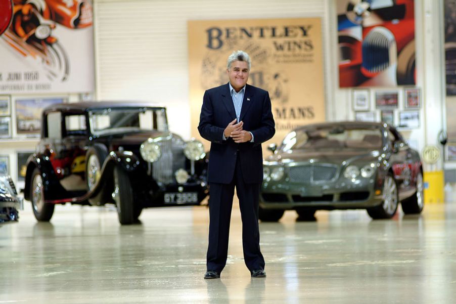 Jay Leno stands in front of 2 of his cars