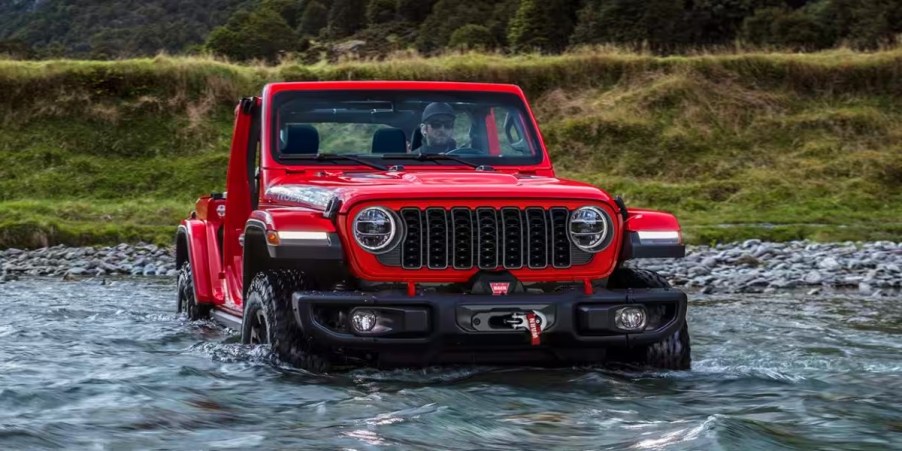 A red Jeep Wrangler small SUV is driving through water.