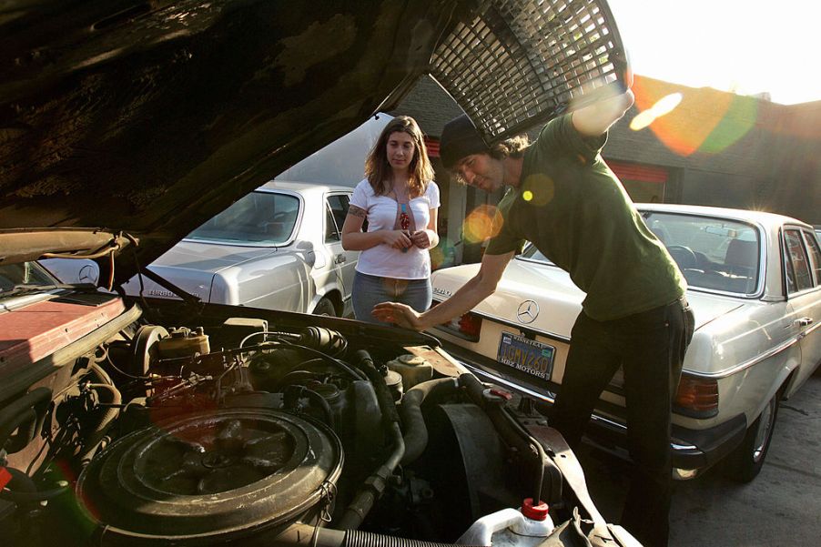 A man looking over his car, getting ready to change his oil during regular maintenance