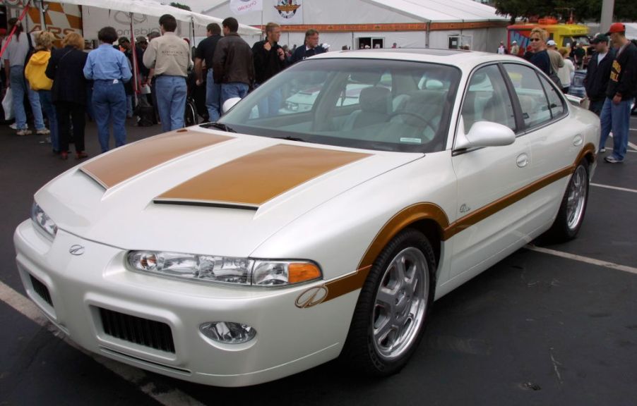 A white 2001 Oldsmobile Intrigue with a tacky body kit is parked at a car show.