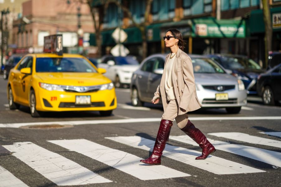 Geraldine Boublil wears sunglasses, a golden necklace, an oversized blazer jacket, a white wool pullover, beige pants, burgundy leather crocodile pattern boots, outside Sies Marjan, during New York Fashion Week Fall Winter 2020