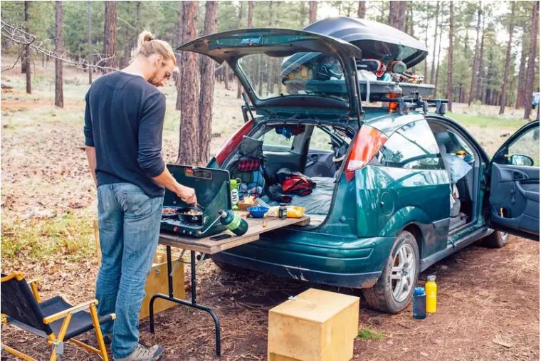 Car camper grilling on a stove off the back of his car