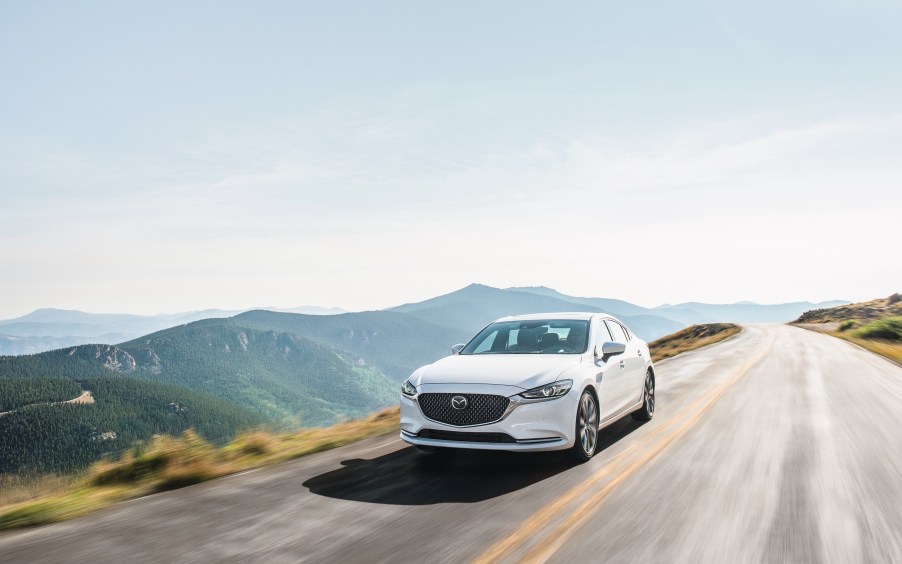 a white mazda6 at speed on a scenic road against a mountainous backdrop