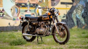 Black-with-yellow-pinstriping 1973 Honda CB350 Four motorcyle parked on lawn in front of artwork