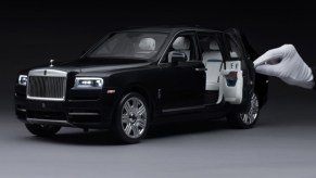 Black 1:8-scale Rolls-Royce Cullinan model with white-gloved hand for scale