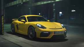 A yellow 2020 Porsche 718 Cayman GT4 drives through a city at night