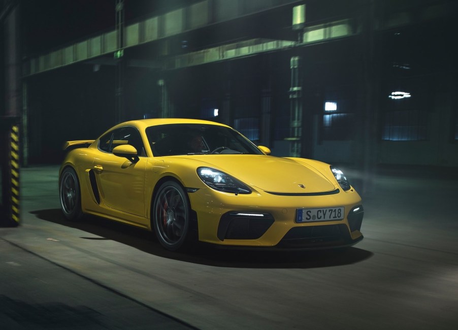 A yellow 2020 Porsche 718 Cayman GT4 drives through a city at night