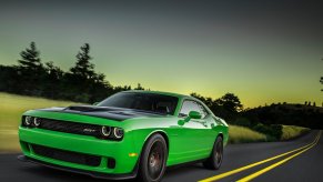 a bright green Dodge Challenger muscle car driving down a scene road at dusk