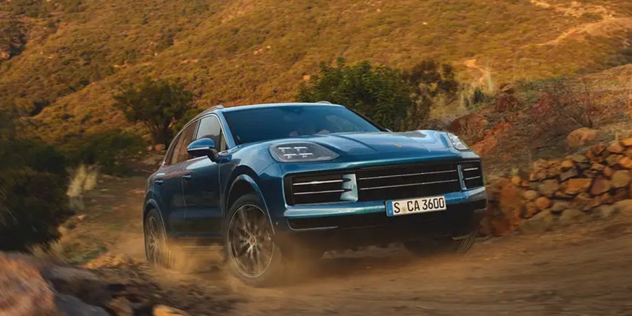 A blue Porsche Cayenne midsize SUV is driving off-road.