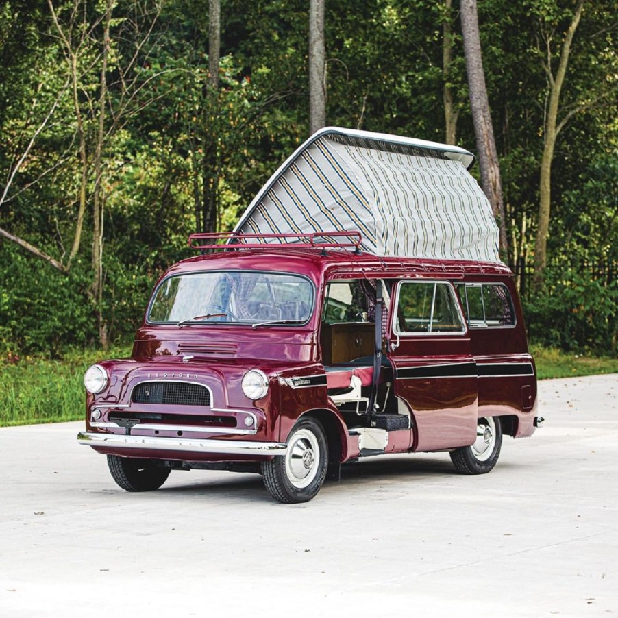 Maroon 1961 Bedford CA Dormobile camper van with its pop-up roof open in front of a forest