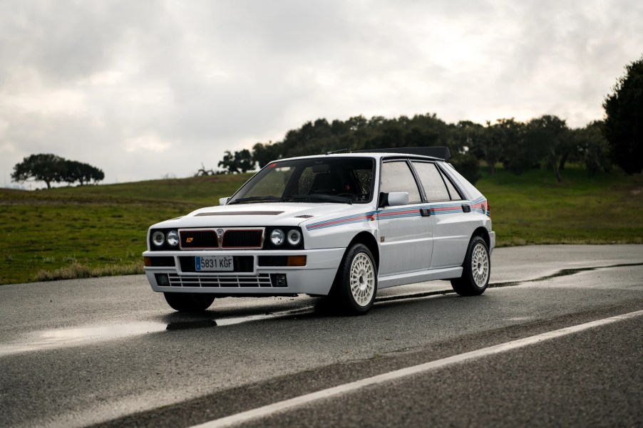 White with red-and-blue stripes 1992 Lancia Delta Integrale Evoluzione I Martini 5 Edition hot hatch on a wet road in front of a grassy hill