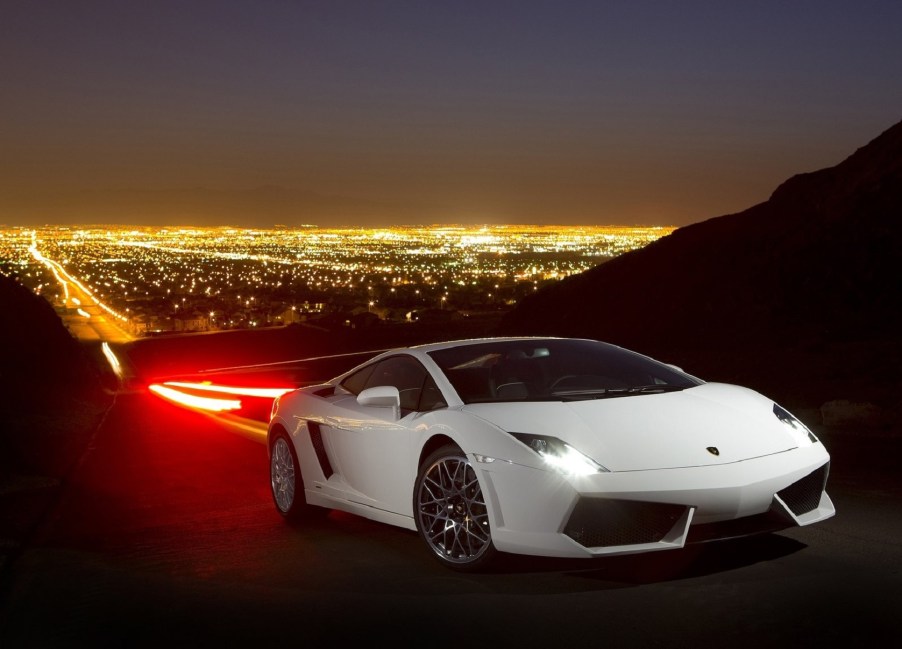 White 2009 Lamborghini Gallardo LP560-4 on a mountain road overlooking a bright-lit city at night