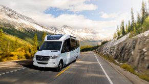 White 2020 Leisure Travel Vans Unity RV driving through a forested mountain road