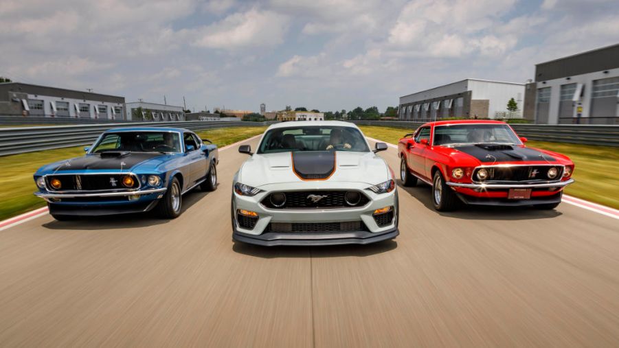 A white 2021 Mustang Mach I flanked by the original 1969 Mach Is in red and blue