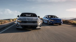 A gray 2021 Kia K5 sedan, the successor to the Kia Optima, is slightly ahead of another in this head-on picture of both cars on the road.