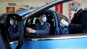 A customer and dealership employee with masks discuss a car in a showroom.