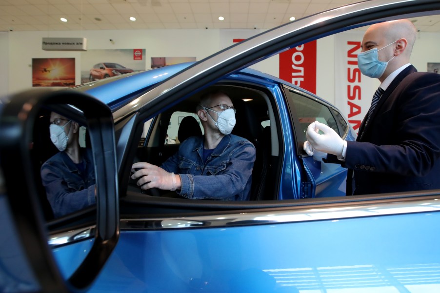 A customer and dealership employee with masks discuss a car in a showroom.