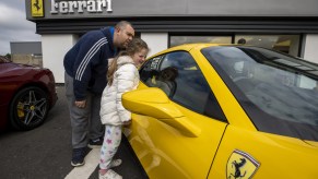 A father and his daughter looking at a new yellow Ferrari