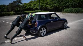 Two team members in team uniform push a blue Mini Cooper through a parking lot.