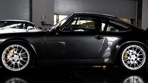 A black Porsche 964 sits in an indoor parking lot.