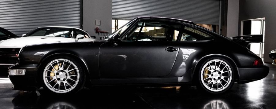 A black Porsche 964 sits in an indoor parking lot.