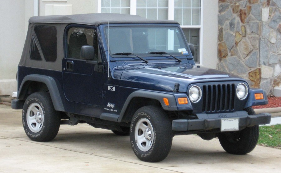 A blue 1990s Jeep Wrangler parked outside of a driveway.