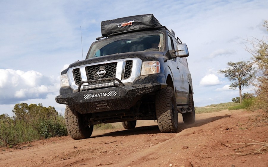 A black, lifted, 4x4, full-size van sits on a dirt road