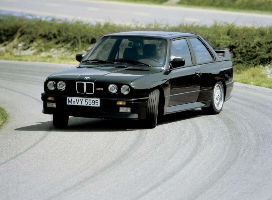 A black 1987 BMW E30 M3 drifting around a racetrack corner