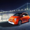 orange Fiat 500e in front of a lit suspension bridge late at night in the city.