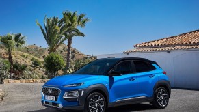 A blue Hyundai Kona Hybrid sits in a driveway lined with palm trees.