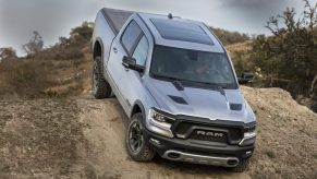 A silver Ram 1500 on a dirt road climbs over the peak of a hill.