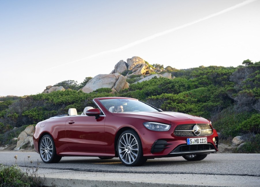 A red 2021 Mercedes E-Class Cabriolet in front of a green-covered rocky hill with its top down