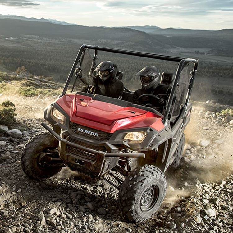 a red Honda UTV Pioneer 1000 LE climbing rocky terrain