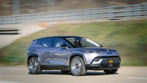 A silver Fisker electric SUV makes a hillside pass.