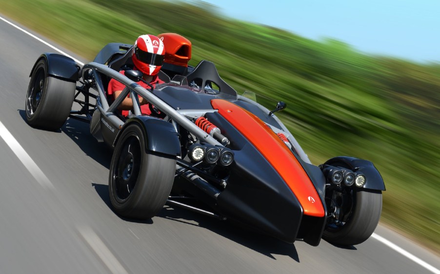 Red Ariel Atom 4 being driven by a helmeted driver down a country road